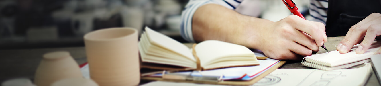 Small business person sitting at desk, working on paperwork. A few of the products they create are sitting in front of them on the desk.