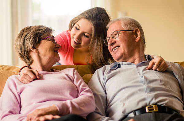 Image of a grandmother and a grandfather sitting on the couch with their granddaughter behind them.